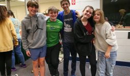Five young people posing together in a room, smiling at the camera.